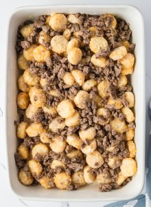 Baked dish with tater tots and crumbled ground meat in a white rectangular casserole dish.