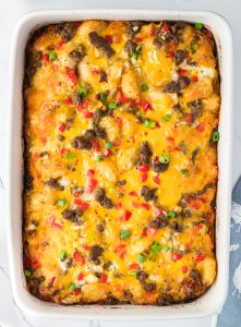 A baked casserole with melted cheese, ground meat, diced red and green peppers, and chopped green onions in a white rectangular dish.