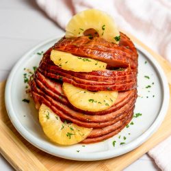 Sliced ham arranged with pineapple rings on a white plate, garnished with herbs, makes for the perfect dish at the office Christmas party.