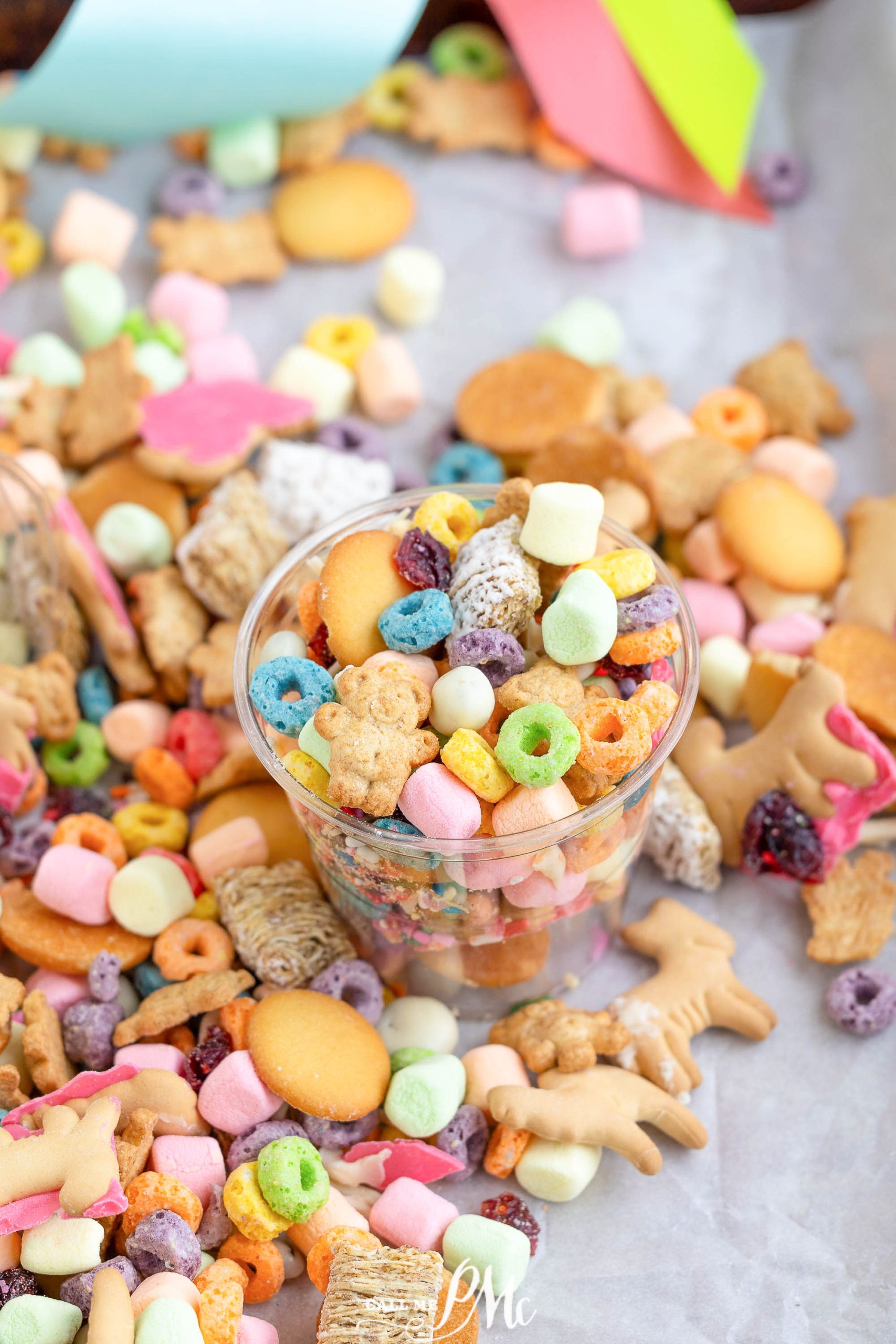 A cup filled with colorful cereals, marshmallows, and various snacks, surrounded by a scattered assortment of similar treats on a surface.