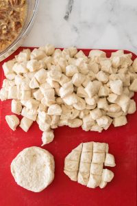 Dough cut into small cubes on a red cutting board, with two uncut pieces of dough nearby.