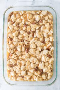 A glass baking dish filled with cubed bread pieces coated in a light brown sauce with pecans.