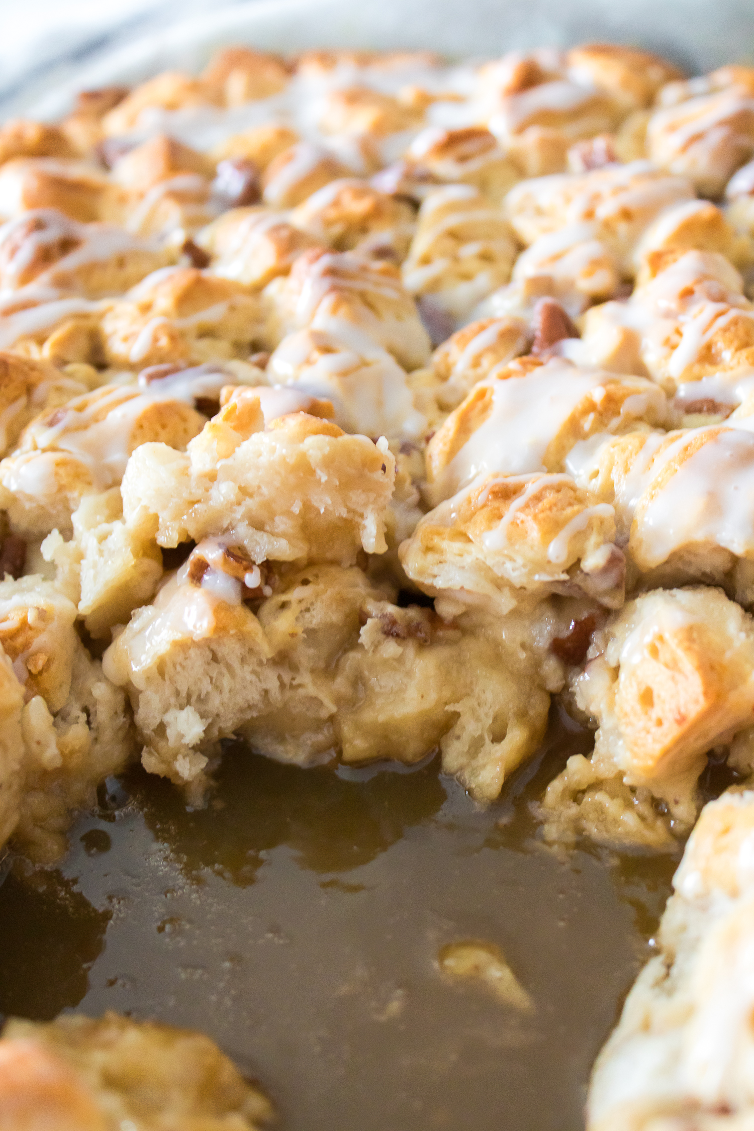 Close-up of a baked dish with pieces of bread drizzled with icing, sitting in a pool of syrup.