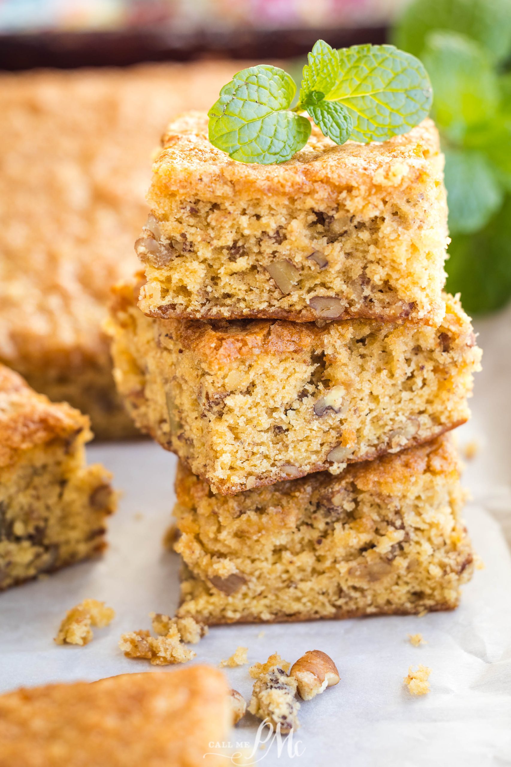 Three stacked pieces of light brown pecan cake with a mint garnish on top.