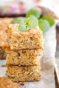 Three stacked squares of walnut cake topped with a mint sprig, displayed on parchment paper.