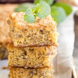 Three stacked squares of walnut cake topped with a mint sprig, displayed on parchment paper.