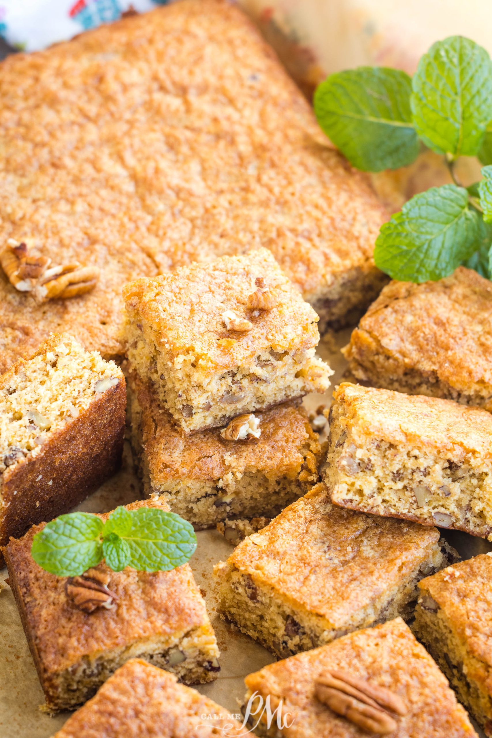 Freshly baked pumpkin pecan bread squares are arranged on a tray, garnished with pecan pieces and mint leaves.