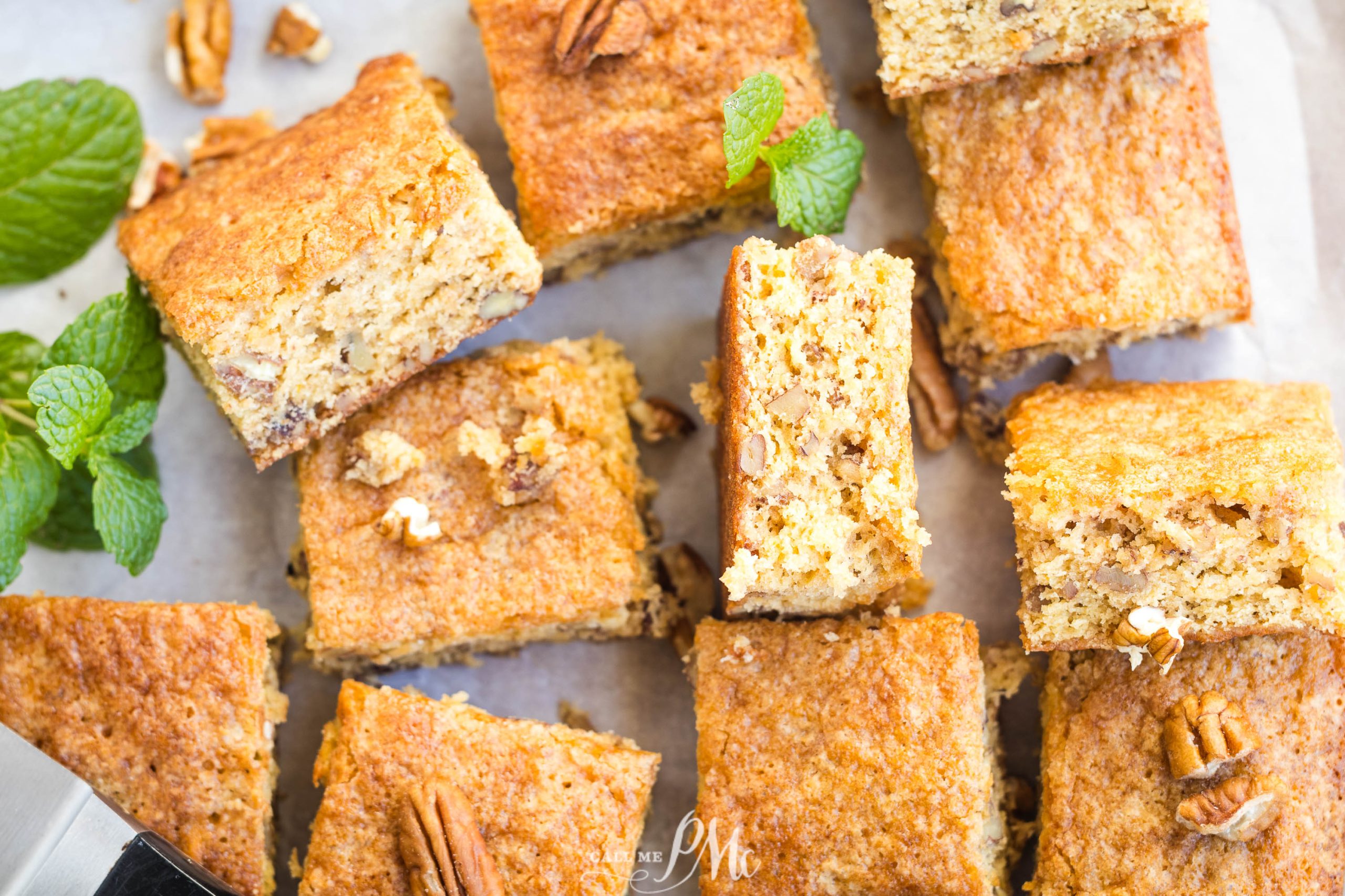 Sliced pieces of banana bread with pecans, garnished with mint leaves on a parchment-lined surface.