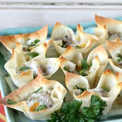 Baked wonton cups filled with a creamy mixture, garnished with fresh parsley, and perfect to make for the office Christmas party, all elegantly arranged on a blue serving tray.