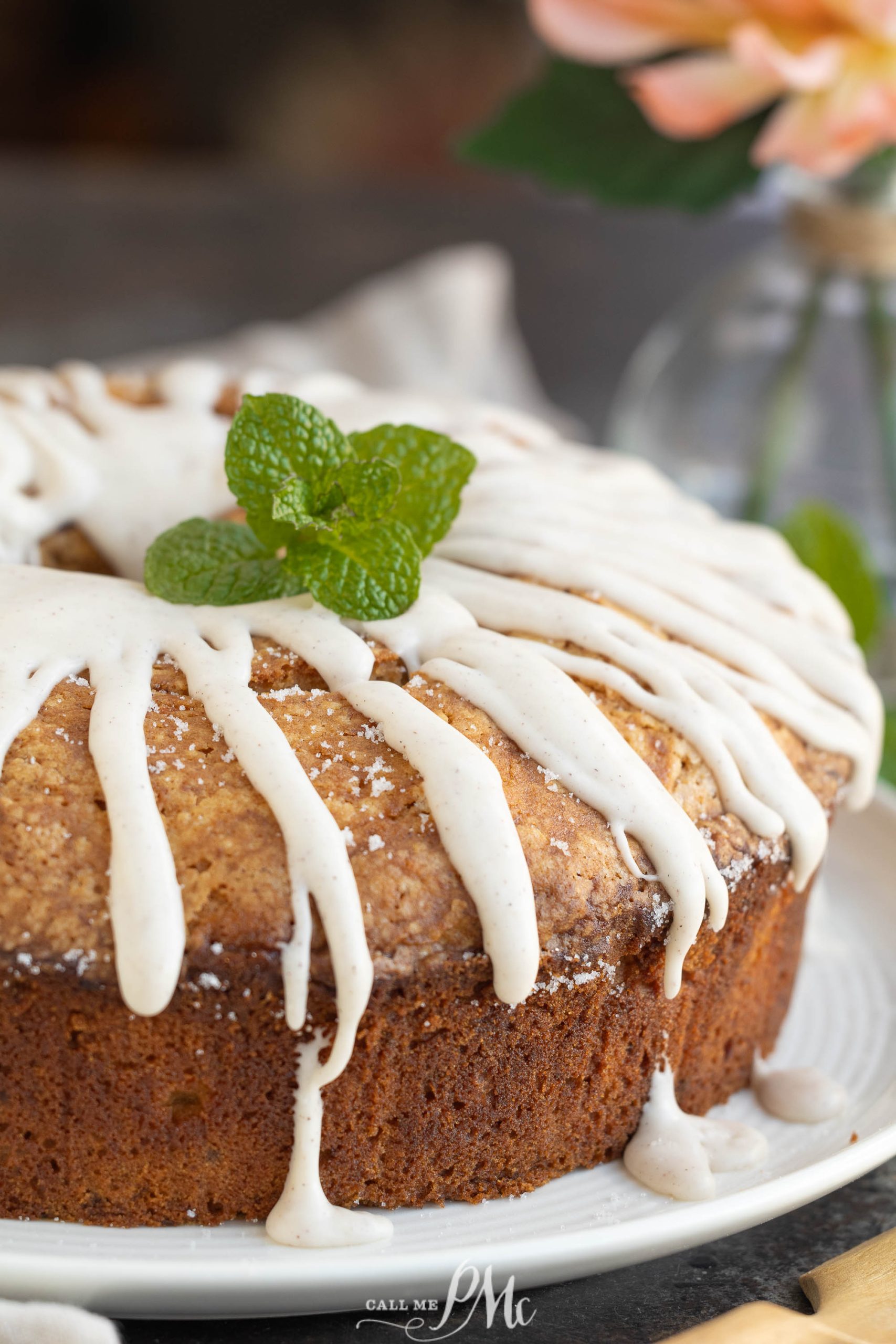 A sweet potato pound cake crowned with white icing and garnished with a sprig of mint, all elegantly presented on a pristine white plate.