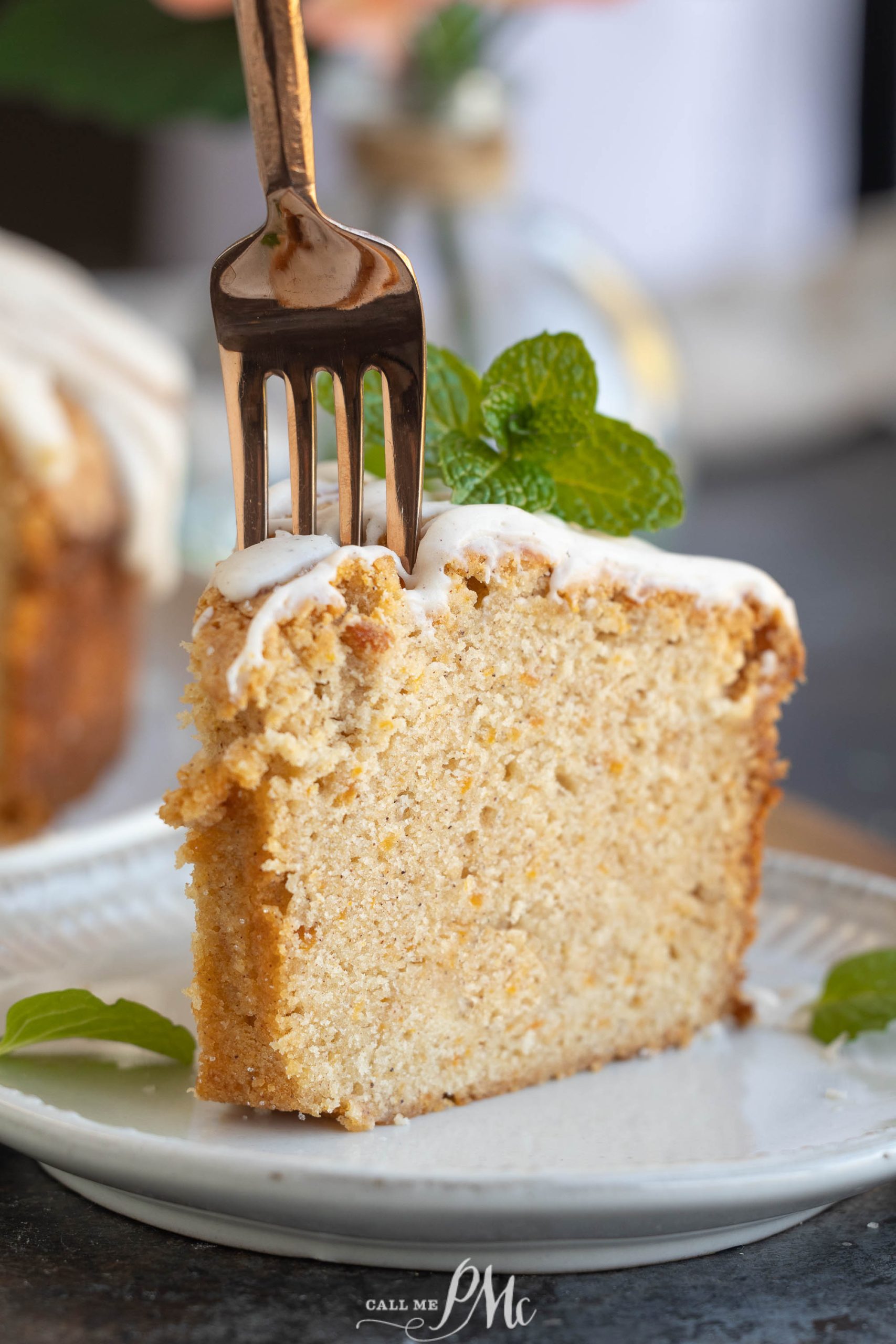 A slice of Sweet Potato Pound Cake with white icing and a mint sprig rests on a plate, invitingly. A fork is inserted into the cake.