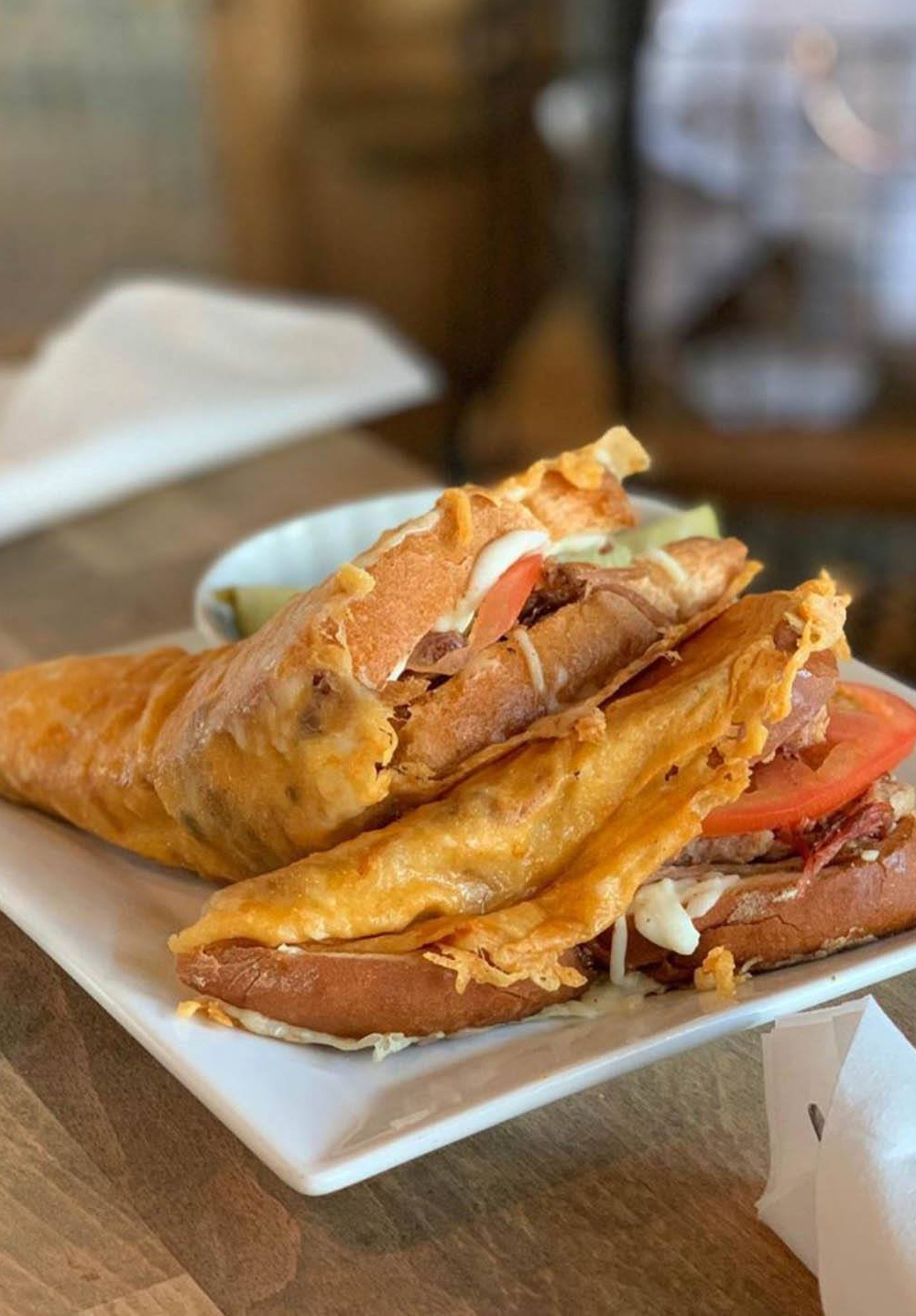 A hot sandwich with melted cheese, tomato slices, and meat on a white plate.