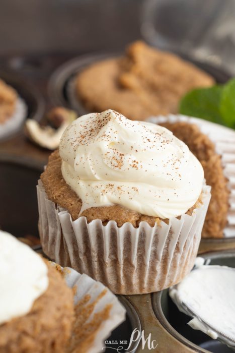 Cupcake with white frosting sprinkled with cinnamon in a white paper liner, placed in a muffin pan.