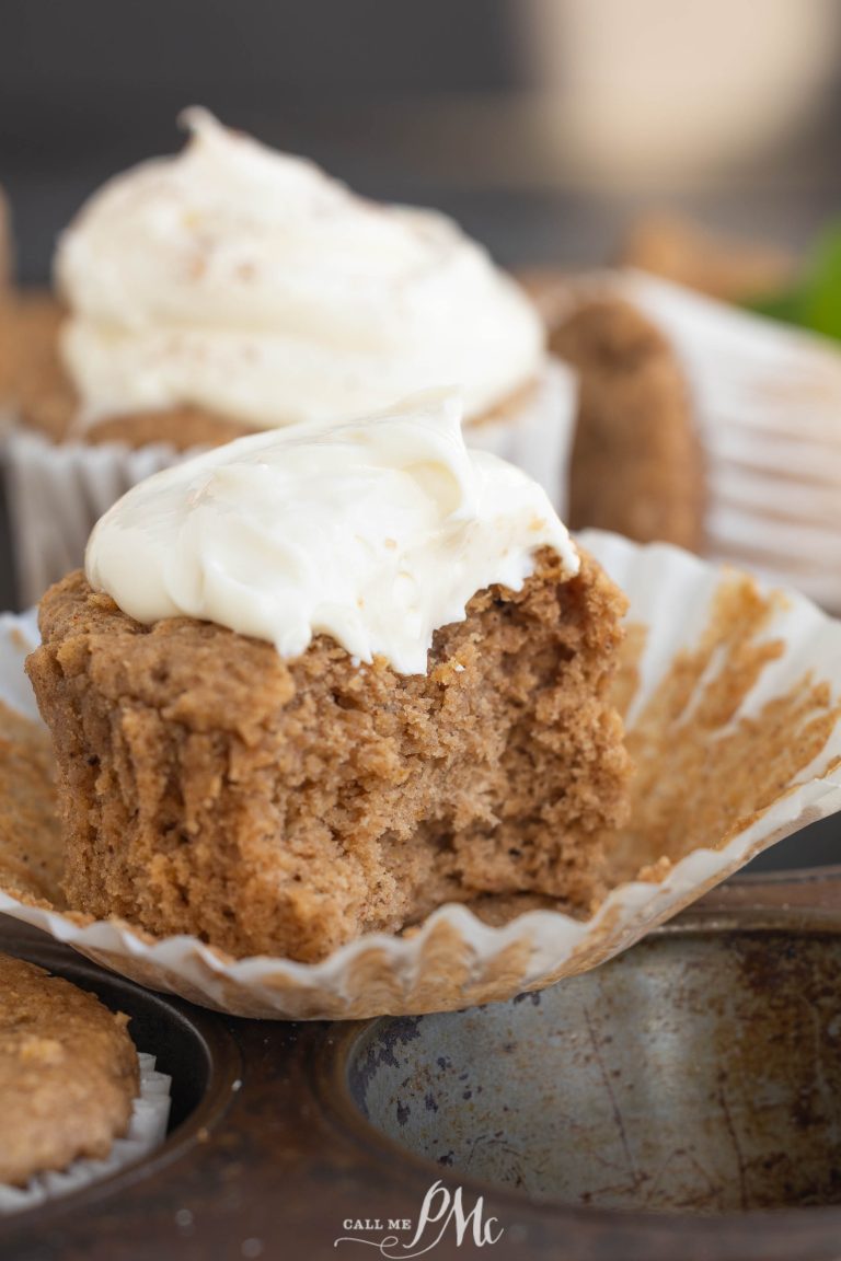 A muffin with cream frosting, partially eaten, sits in an unwrapped paper liner in a muffin tray.