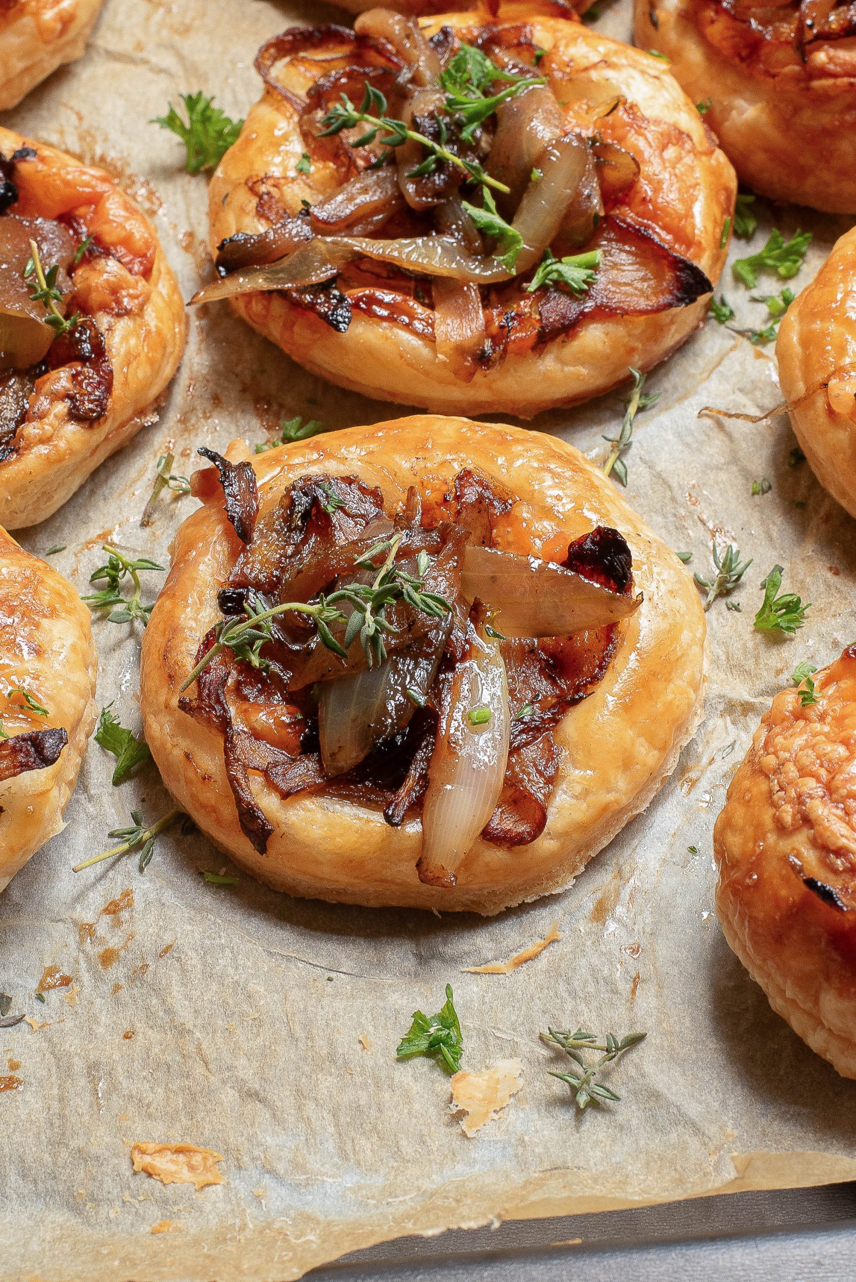 Puff pastries topped with caramelized onions and herbs on a baking sheet lined with parchment paper.