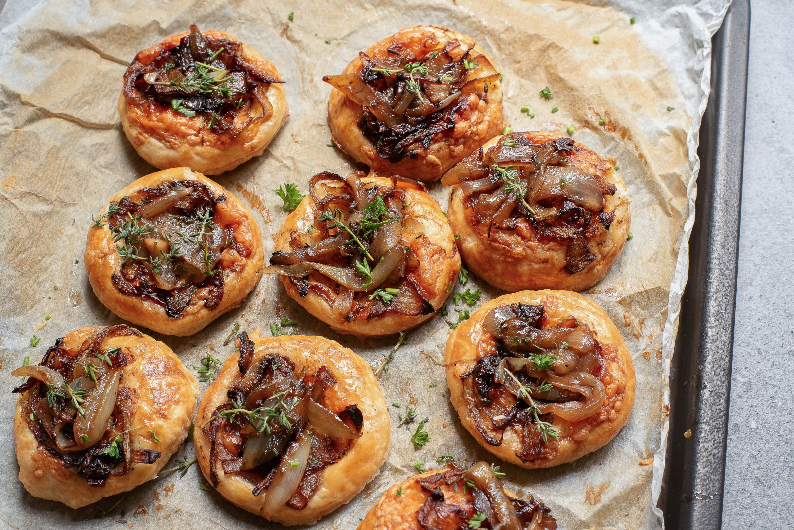 Eight onion and herb puff pastries on a parchment-lined baking tray.