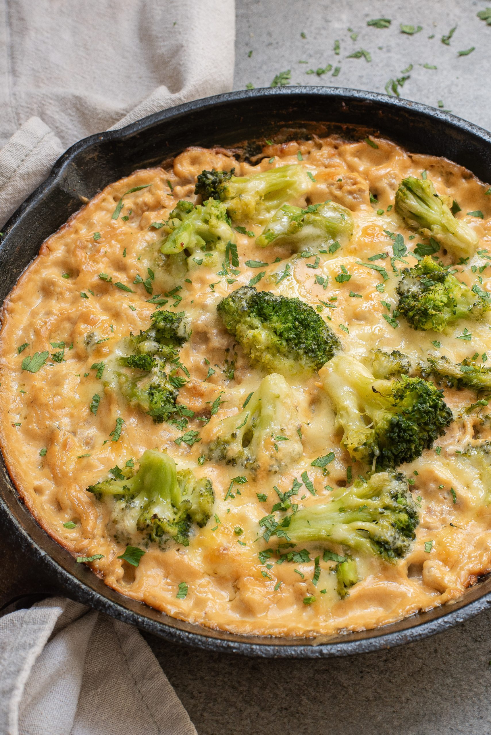 Cheesy broccoli and pasta casserole in a cast iron skillet, garnished with herbs.