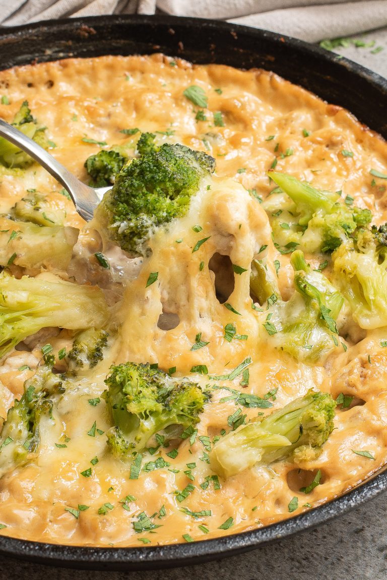 A skillet filled with cheesy broccoli and rice casserole, topped with melted cheese and parsley. A spoon is lifting a portion from the dish.