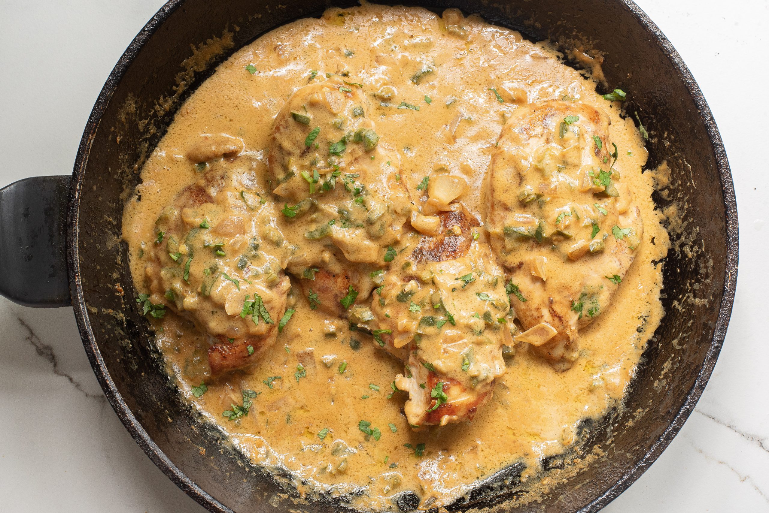 Chicken breasts in a creamy mushroom sauce with herbs are cooking in a black skillet.