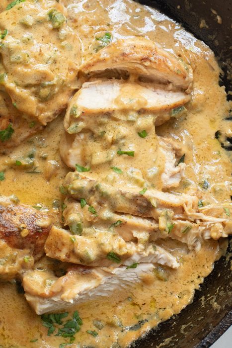 Sliced chicken breast covered in a creamy yellow sauce with herbs, served in a black pan.