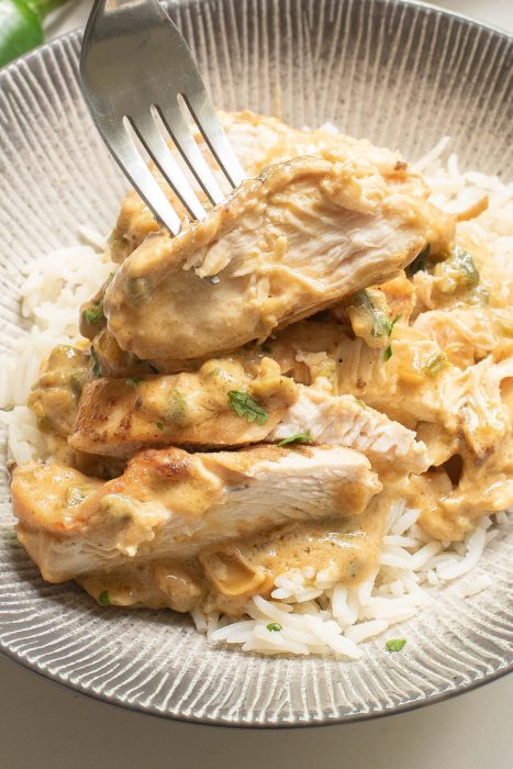 Fork piercing Keto Jalapeno Cheesy Chicken over white rice on a textured plate.