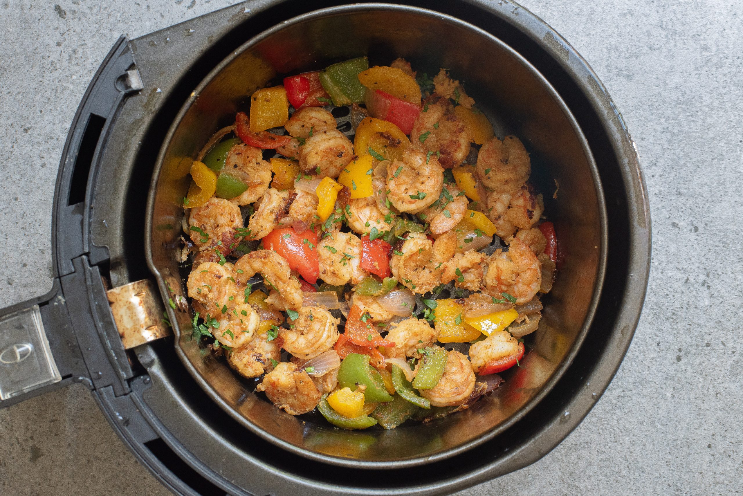 Cooked Keto Fajita Shrimp Dinner with bell peppers and onions in an air fryer basket on a gray surface.