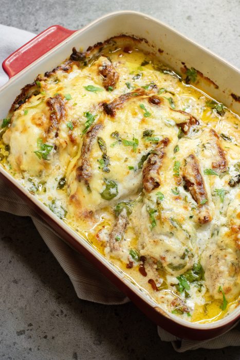 Baked Tuscan chicken casserole  in a red dish topped with melted cheese, herbs, and green seasoning.