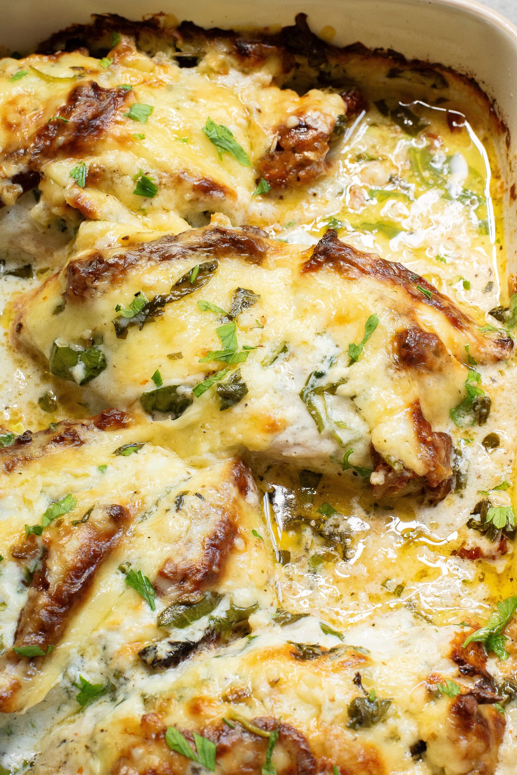 Baked Tuscan chicken casserole covered in melted cheese and herbs, garnished with fresh parsley in a baking dish.