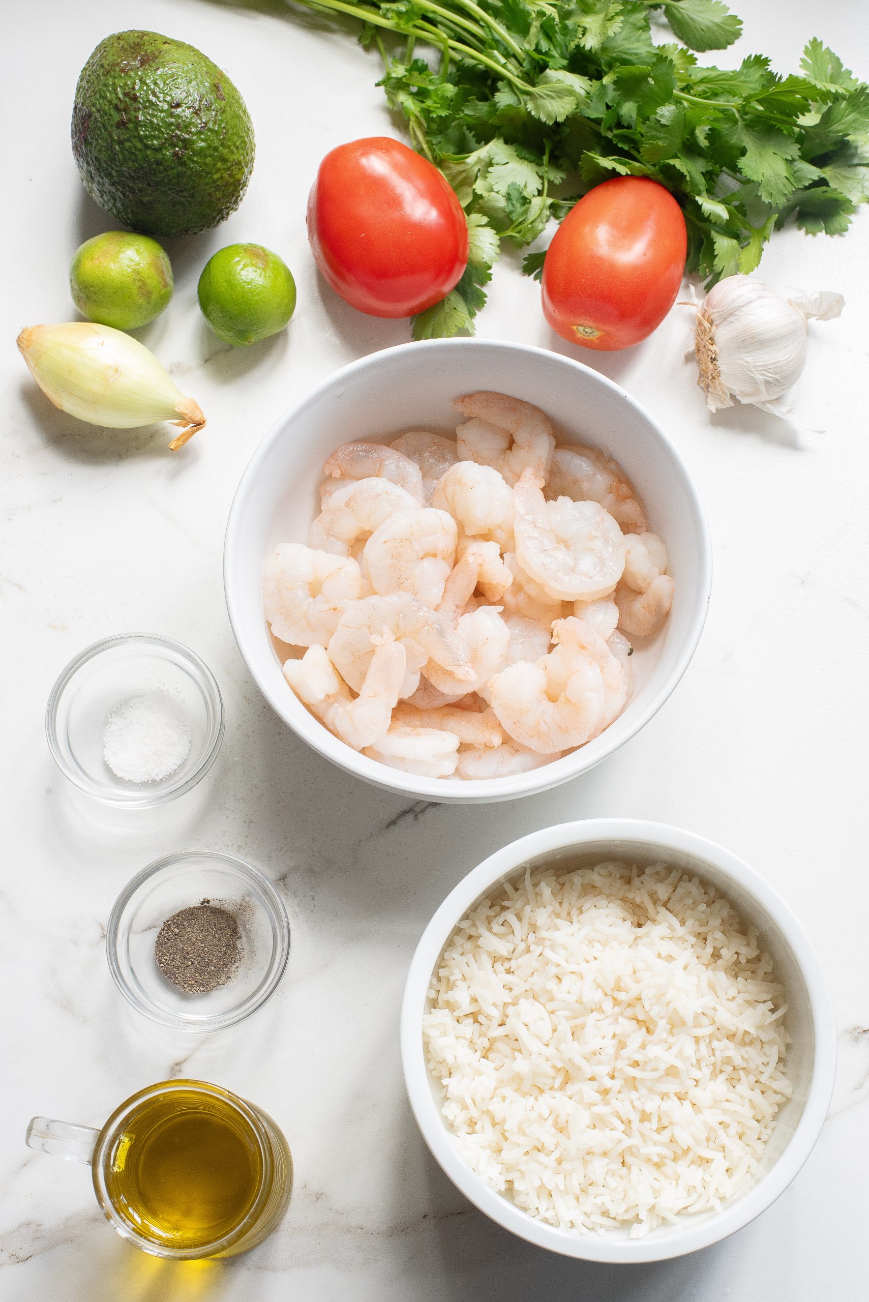 Ingredients on a countertop: shrimp, rice, avocado, lime, tomato, garlic, cilantro, onion, salt, pepper, and olive oil.