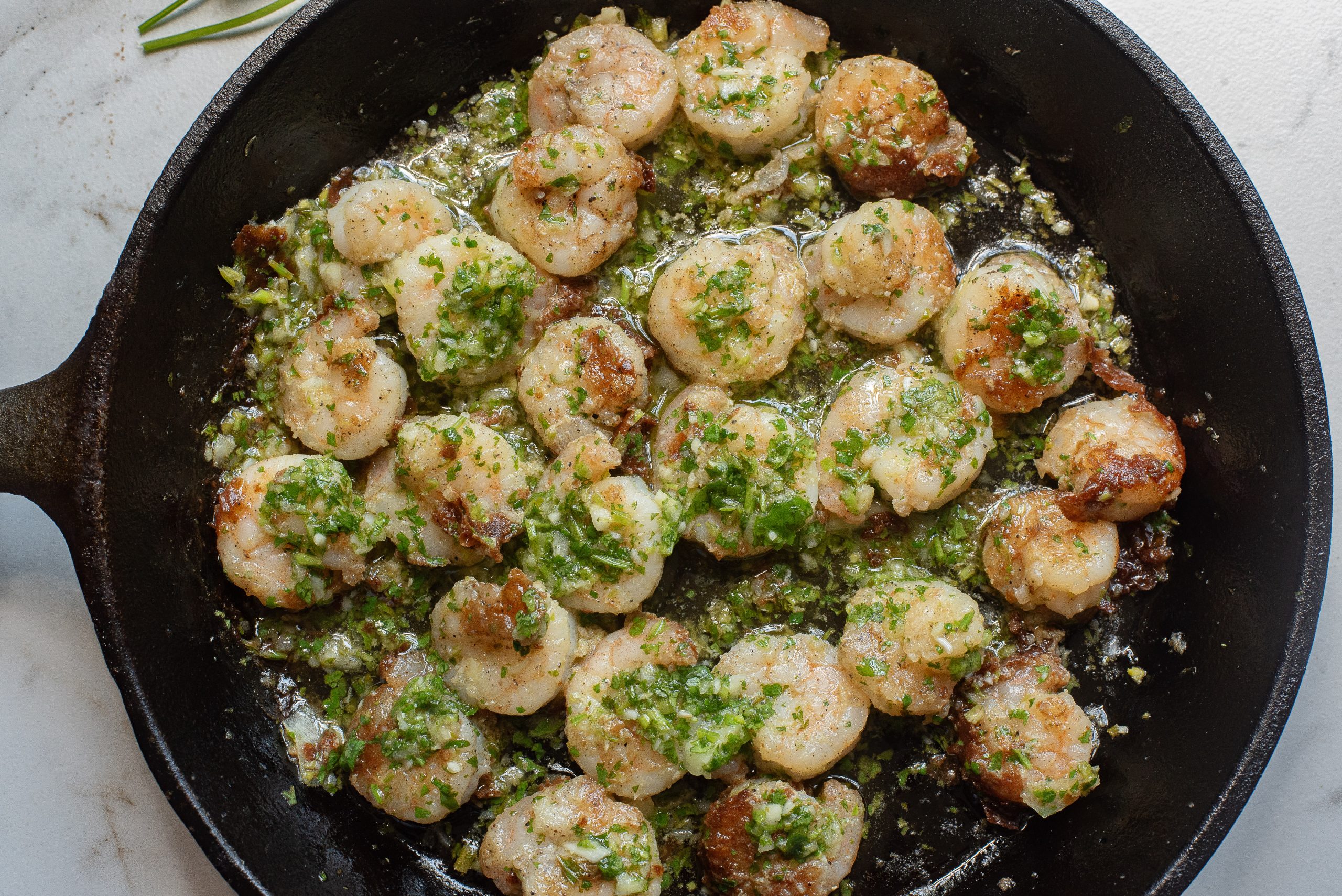 Scallops being cooked in a black skillet, garnished with chopped herbs and a light sauce.