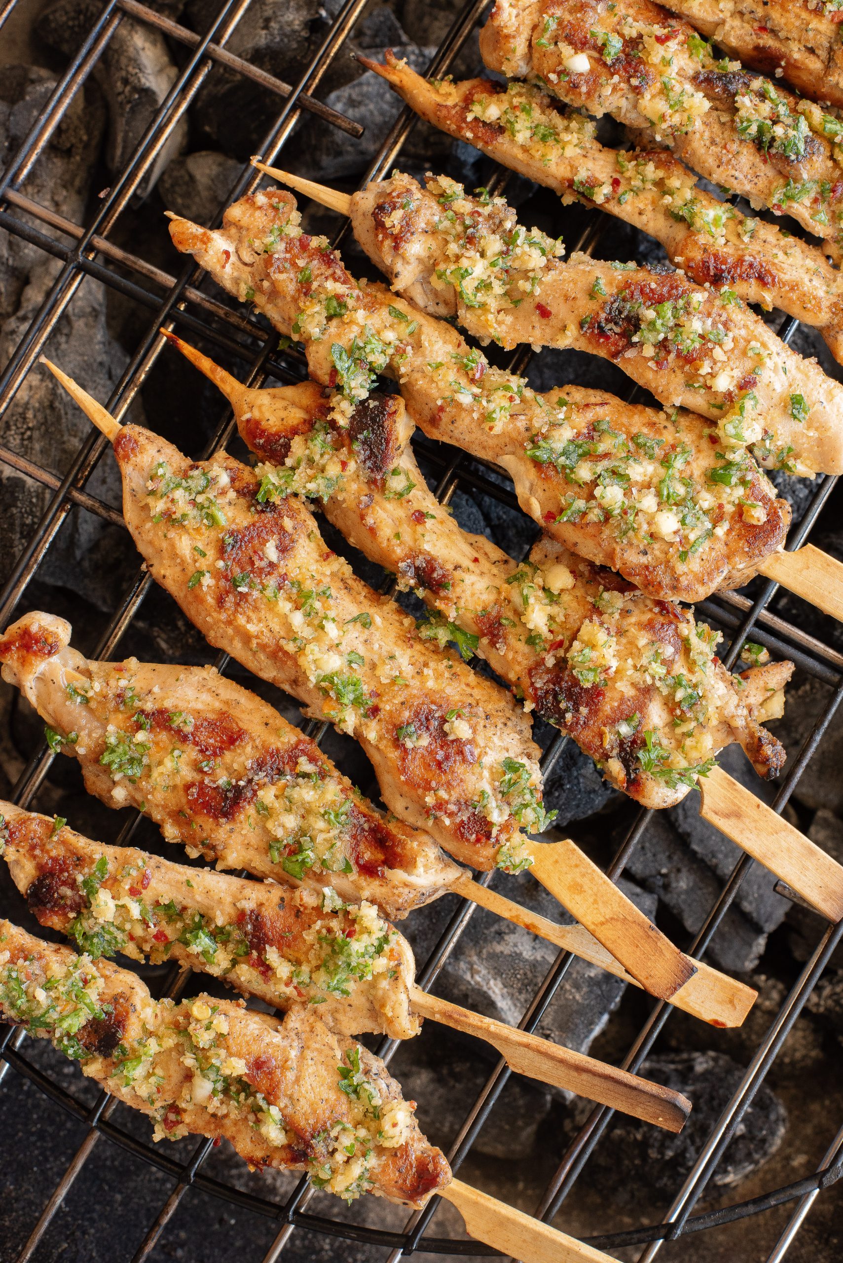 Grilled chicken skewers with herbs and spices on a metal grate over hot coals.