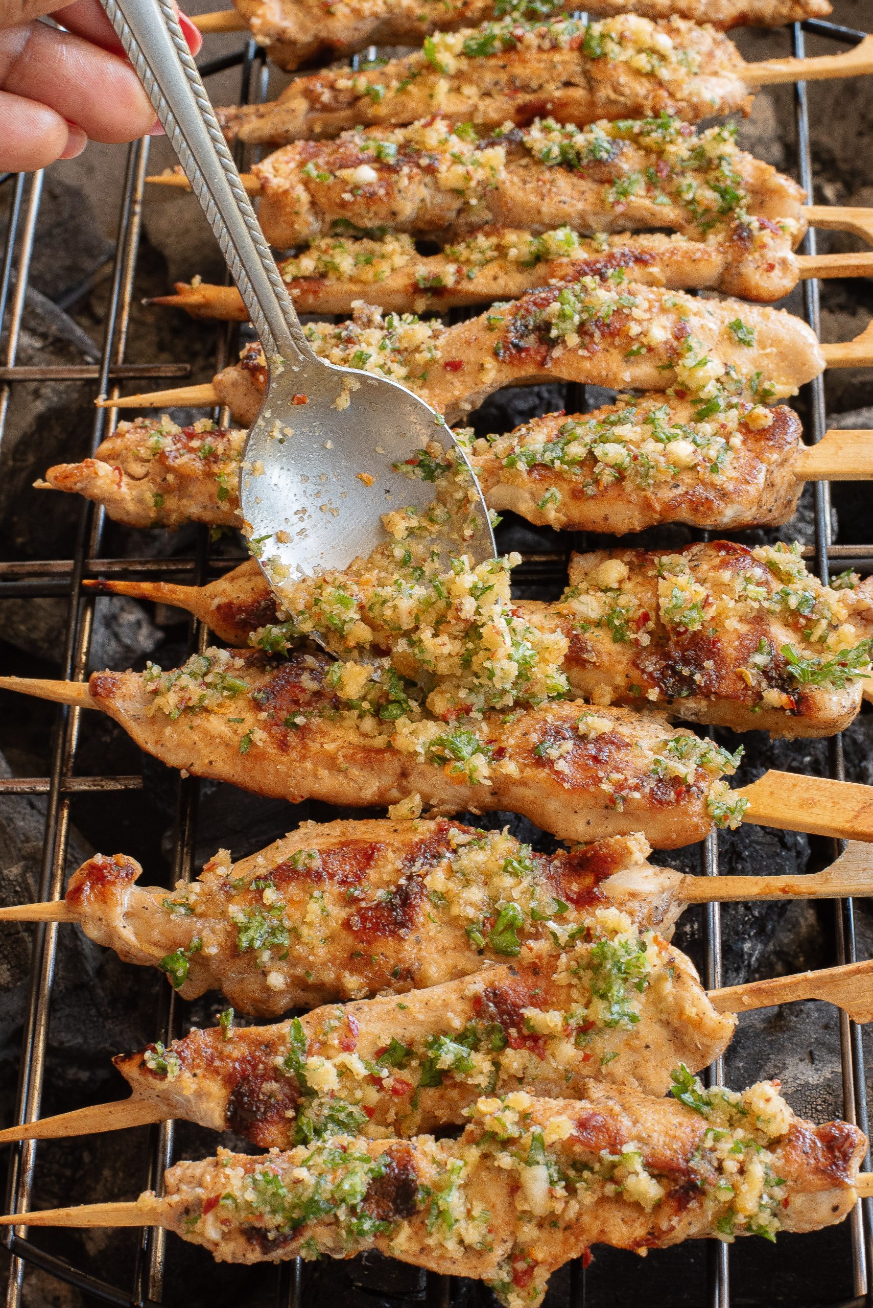 Chicken skewers being seasoned with a garlic and herb mixture on a grill.