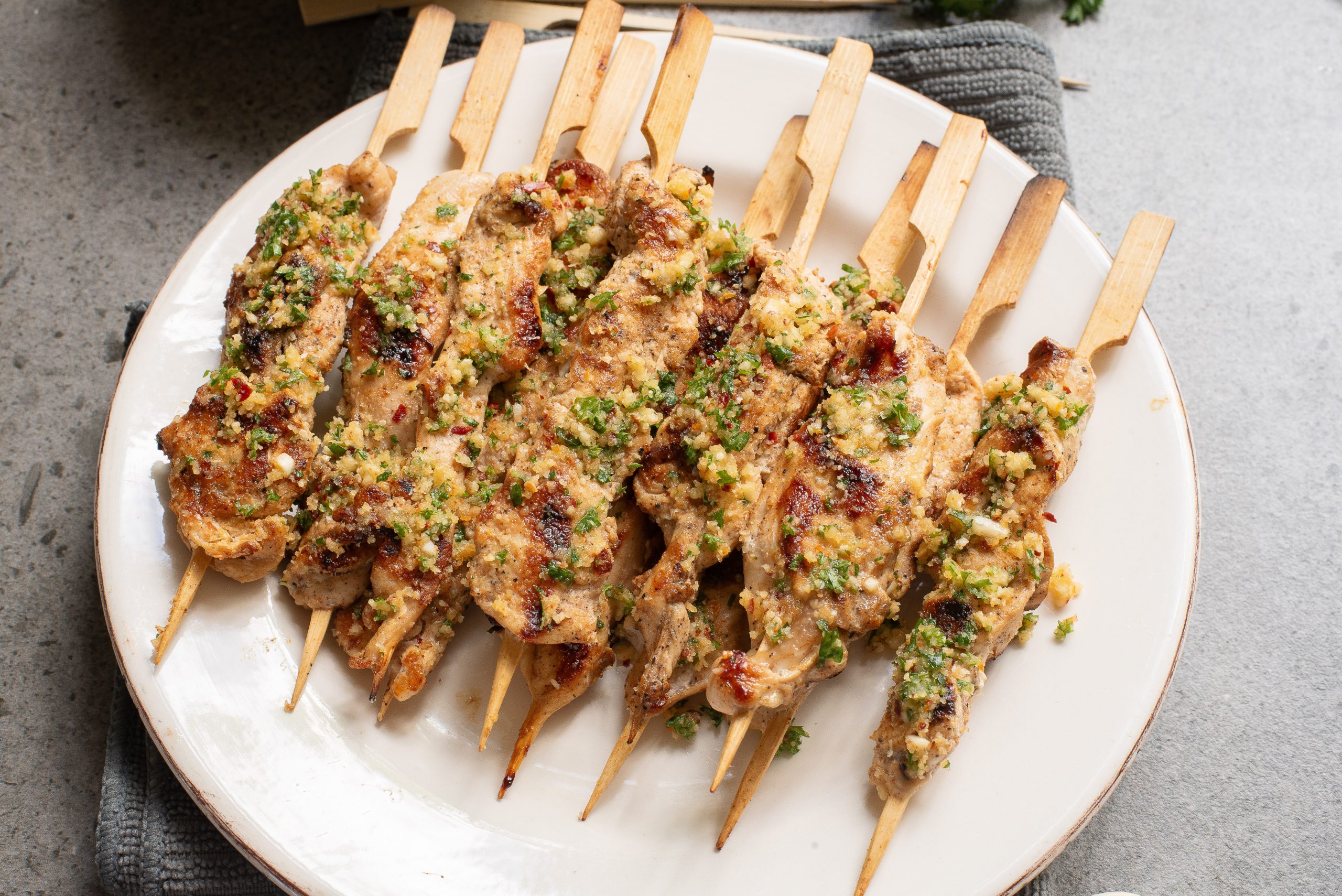 A plate of grilled chicken skewers garnished with herbs and spices, placed on a gray surface.