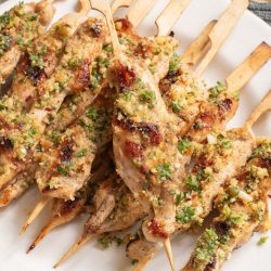 Grilled chicken skewers with herbs and breadcrumbs on a white plate.