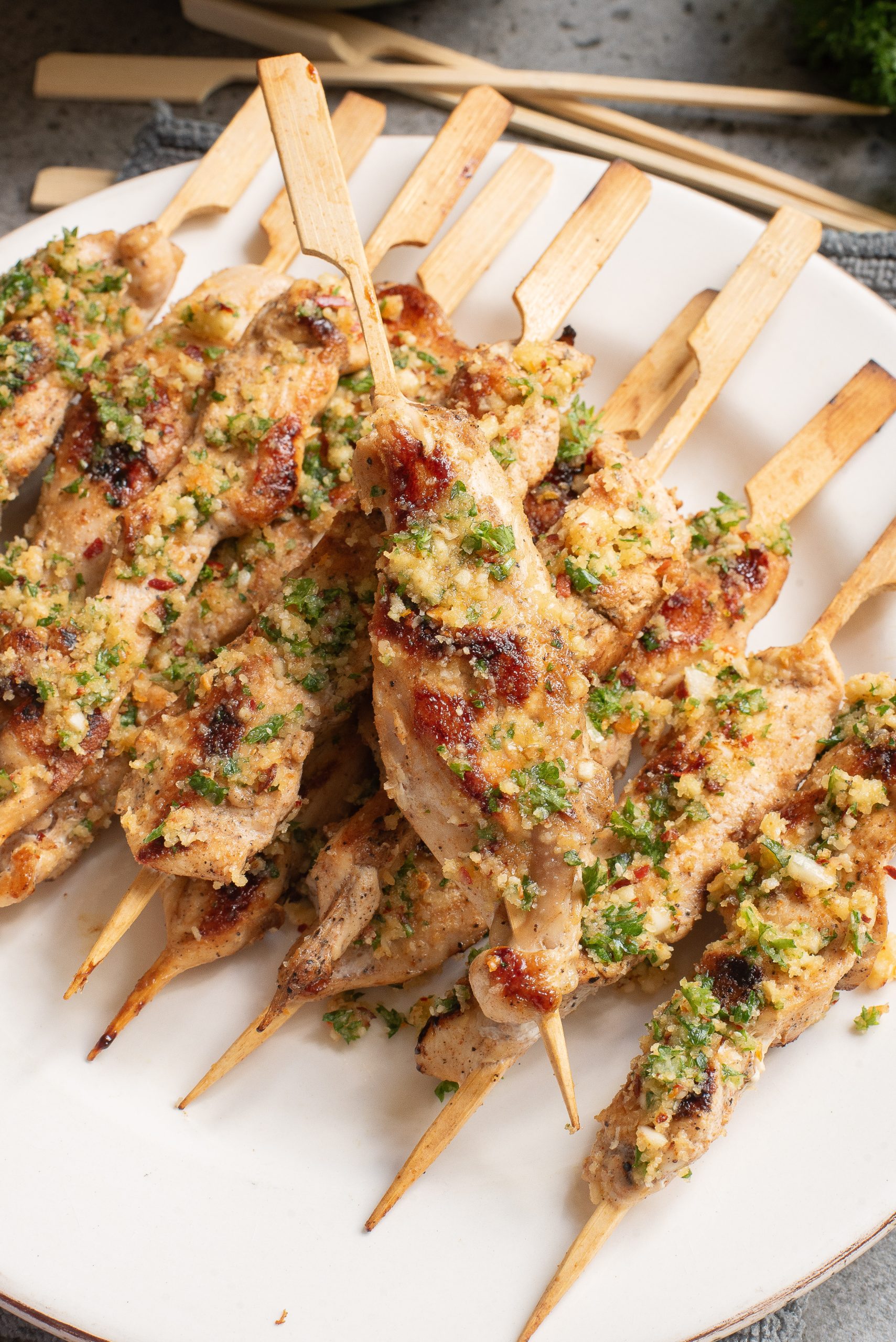 Grilled chicken skewers with herbs and breadcrumbs on a white plate.