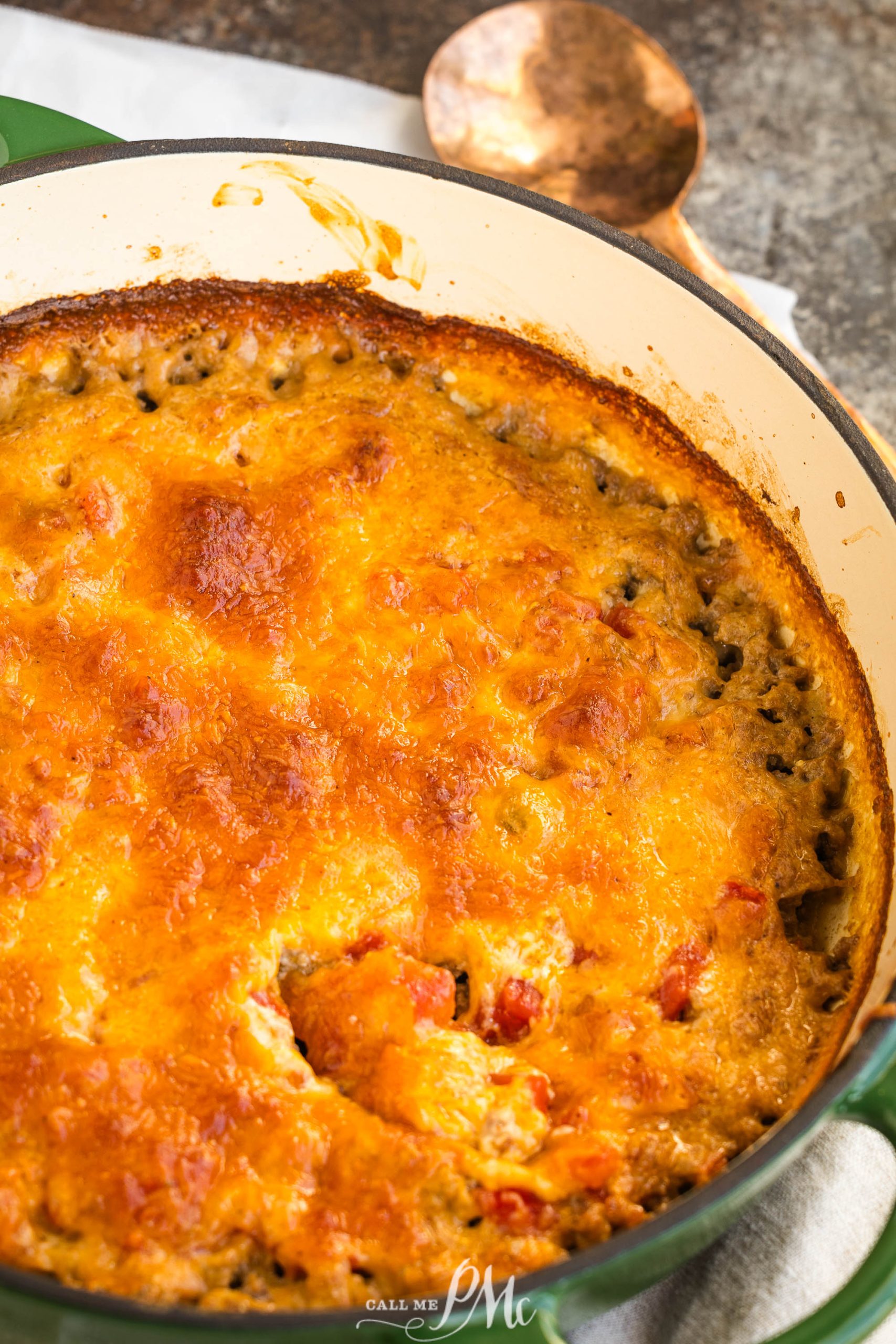 Cheesy Keto hamburger casserole in a green dish, with a golden-brown crust. A vintage wooden spoon is beside the dish on a cloth.