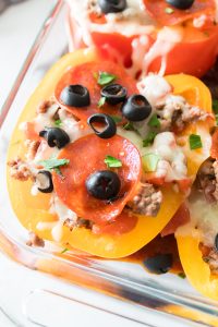 Bell peppers stuffed with ground meat, topped with sliced pepperoni, black olives, melted cheese, and fresh parsley in a glass dish.