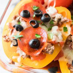 Bell peppers stuffed with ground meat, topped with sliced pepperoni, black olives, melted cheese, and fresh parsley in a glass dish.