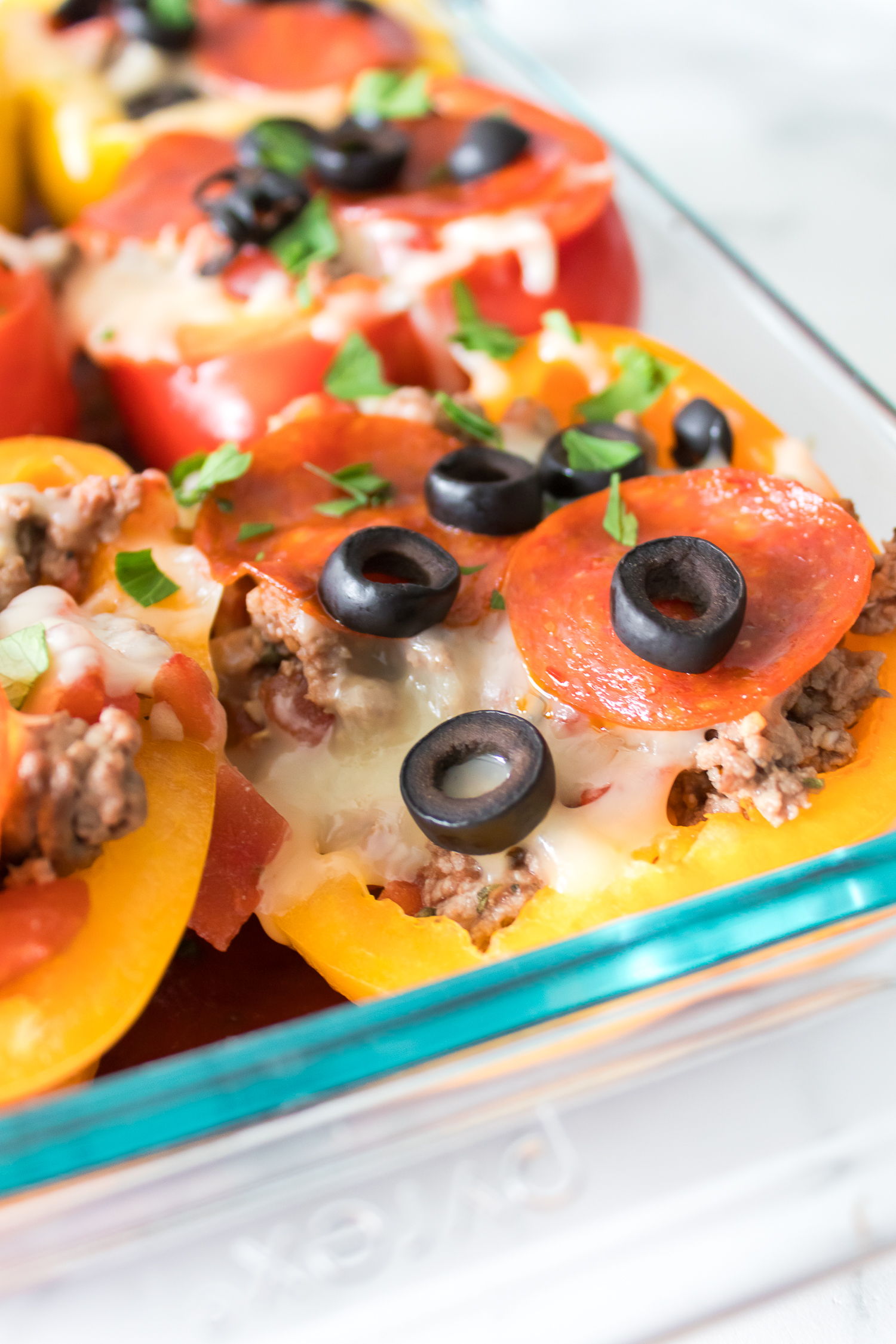 A glass dish containing stuffed bell peppers topped with melted cheese, pepperoni, sliced black olives, and garnished with fresh parsley.