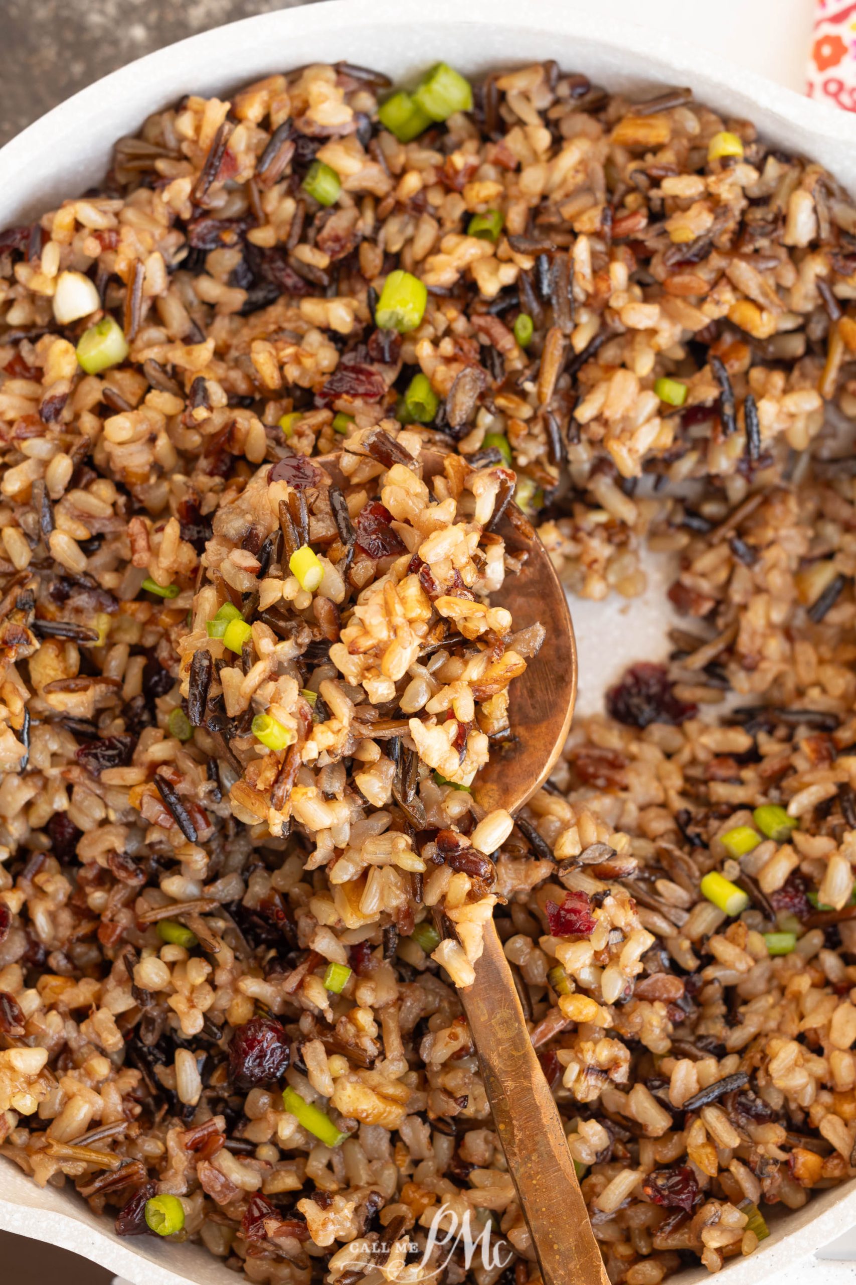 A bowl of food with chopped green onions and cranberries, stirred with a wooden spoon.