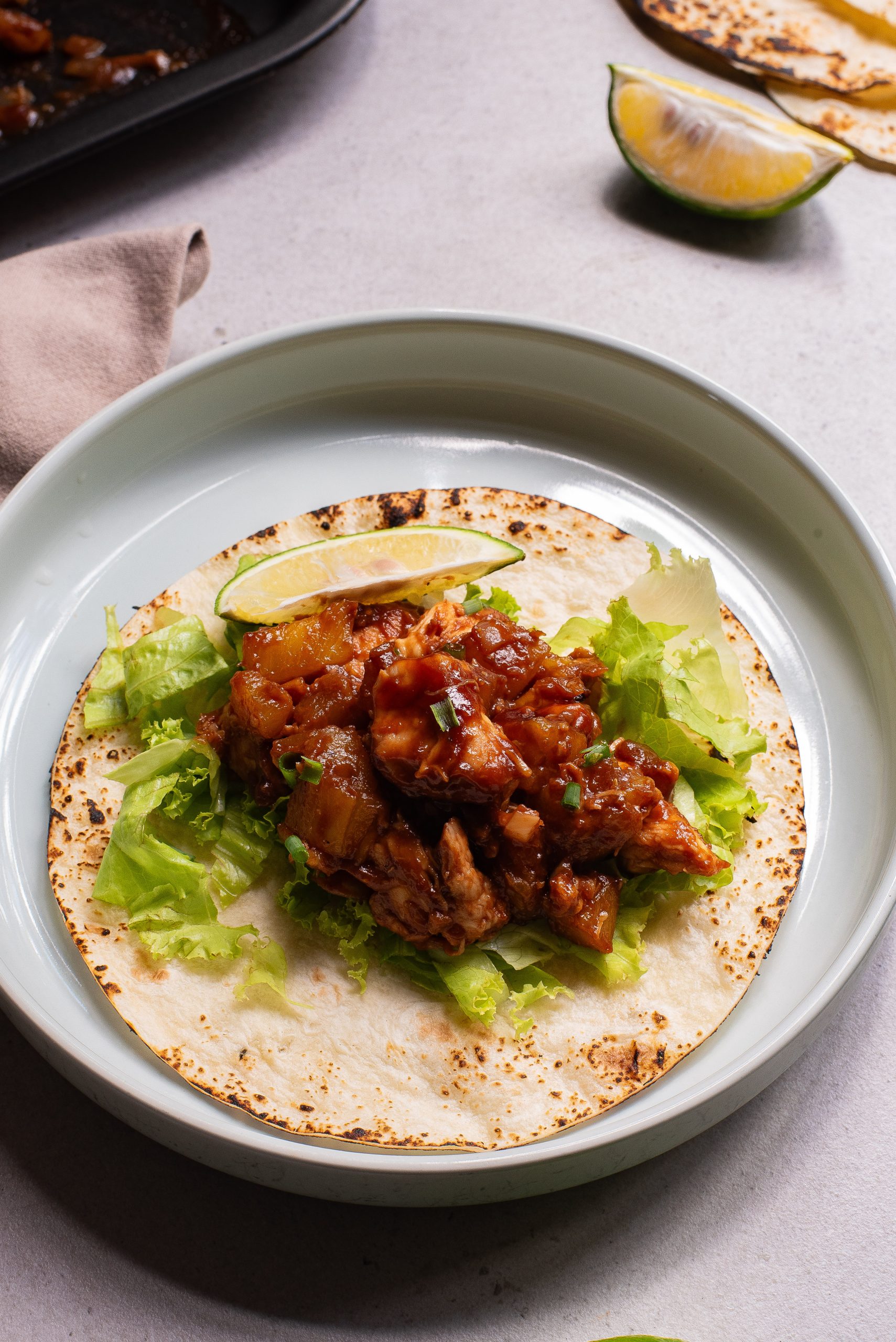 A BBQ Chicken Sheet Pan Tacos on a plate topped with lettuce, diced meat, and salsa, garnished with a lime wedge.