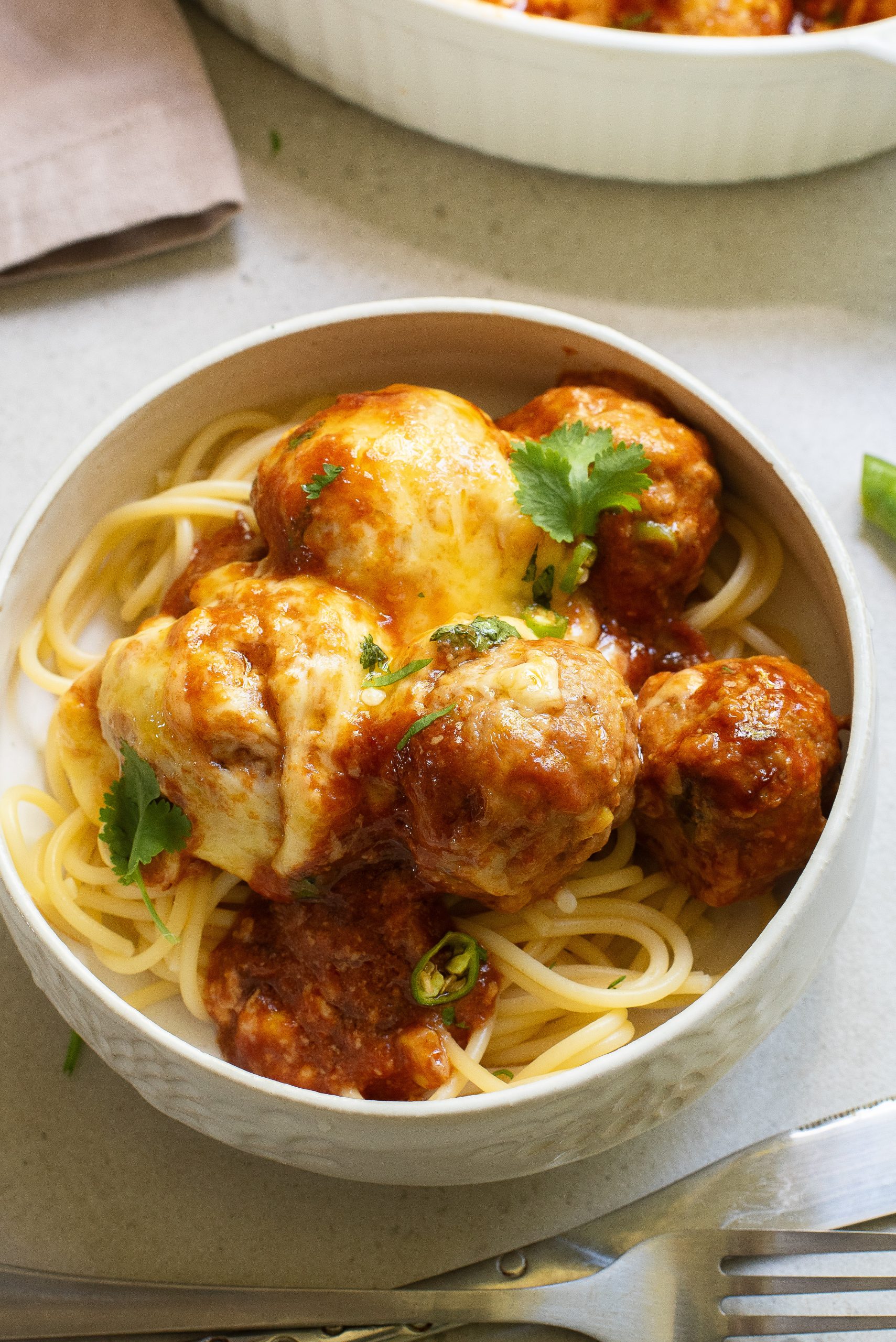 A bowl of spaghetti topped with meatballs, tomato sauce, and melted cheese, garnished with cilantro.