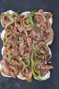 Open-faced sandwich topped with sliced beef, green bell peppers, and mushrooms in a brown sauce.