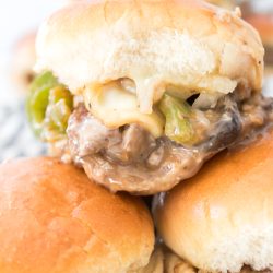 Close-up of stacked sliders with cheese, beef, and green peppers on soft buns.