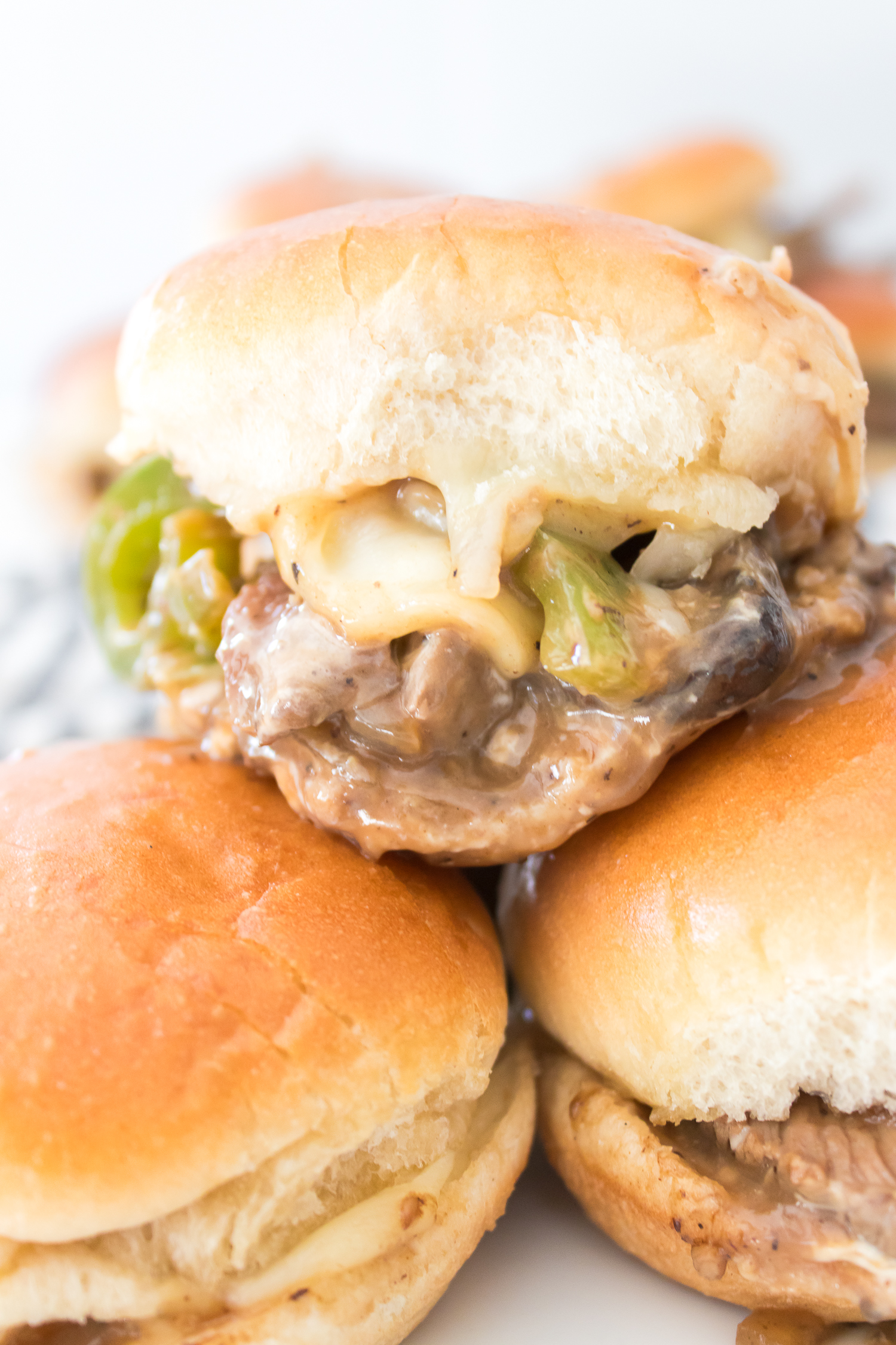 Close-up of stacked sliders with cheese, beef, and green peppers on soft buns.