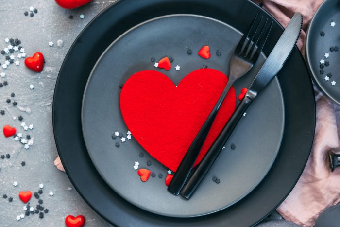 A red heart-shaped decoration on a dark plate with a fork and knife, surrounded by small heart and star confetti.