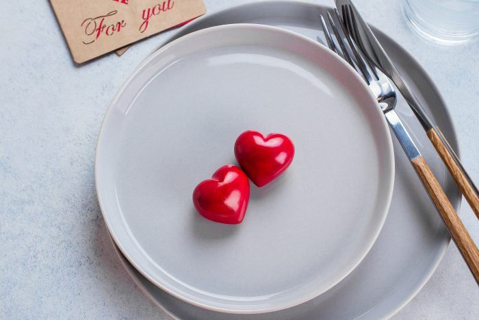 Two red heart-shaped objects on stacked gray plates with a fork and knife. A card with "For you" is in the background.