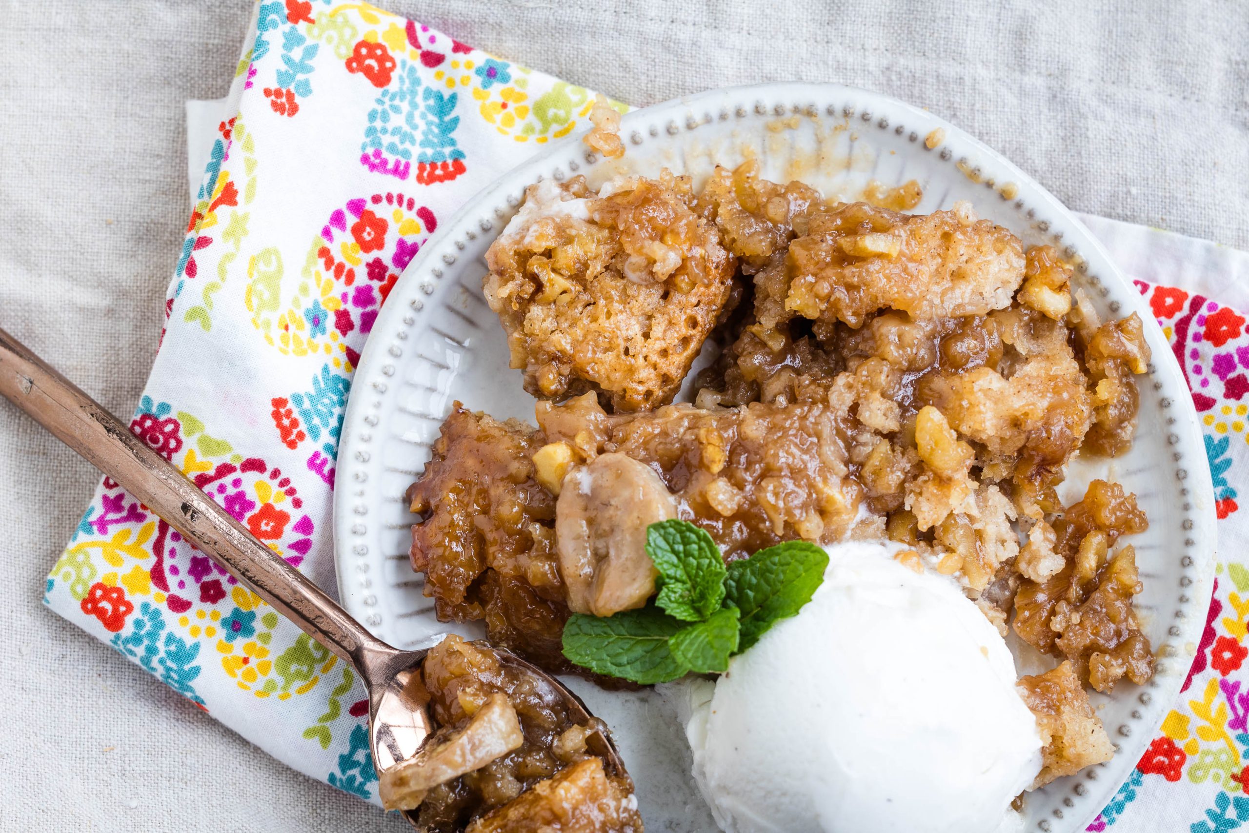 A plate of bread pudding topped with banana slices and a scoop of vanilla ice cream, garnished with mint, on a colorful napkin.