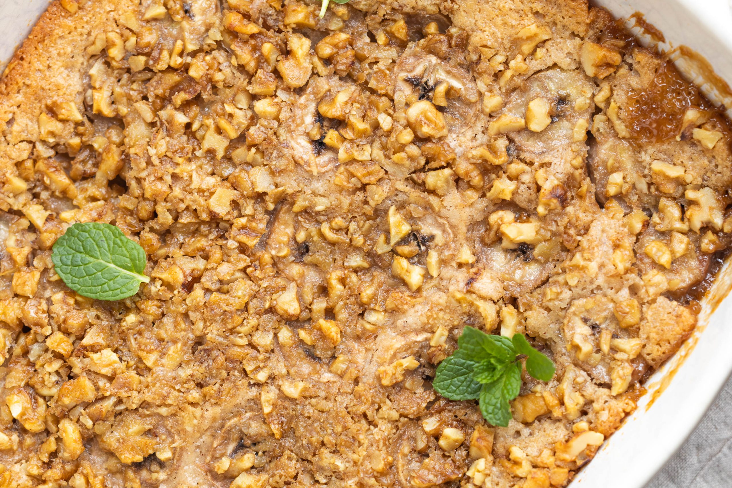 Close-up of a baked dessert topped with crumbled nuts and garnished with two small mint leaves.