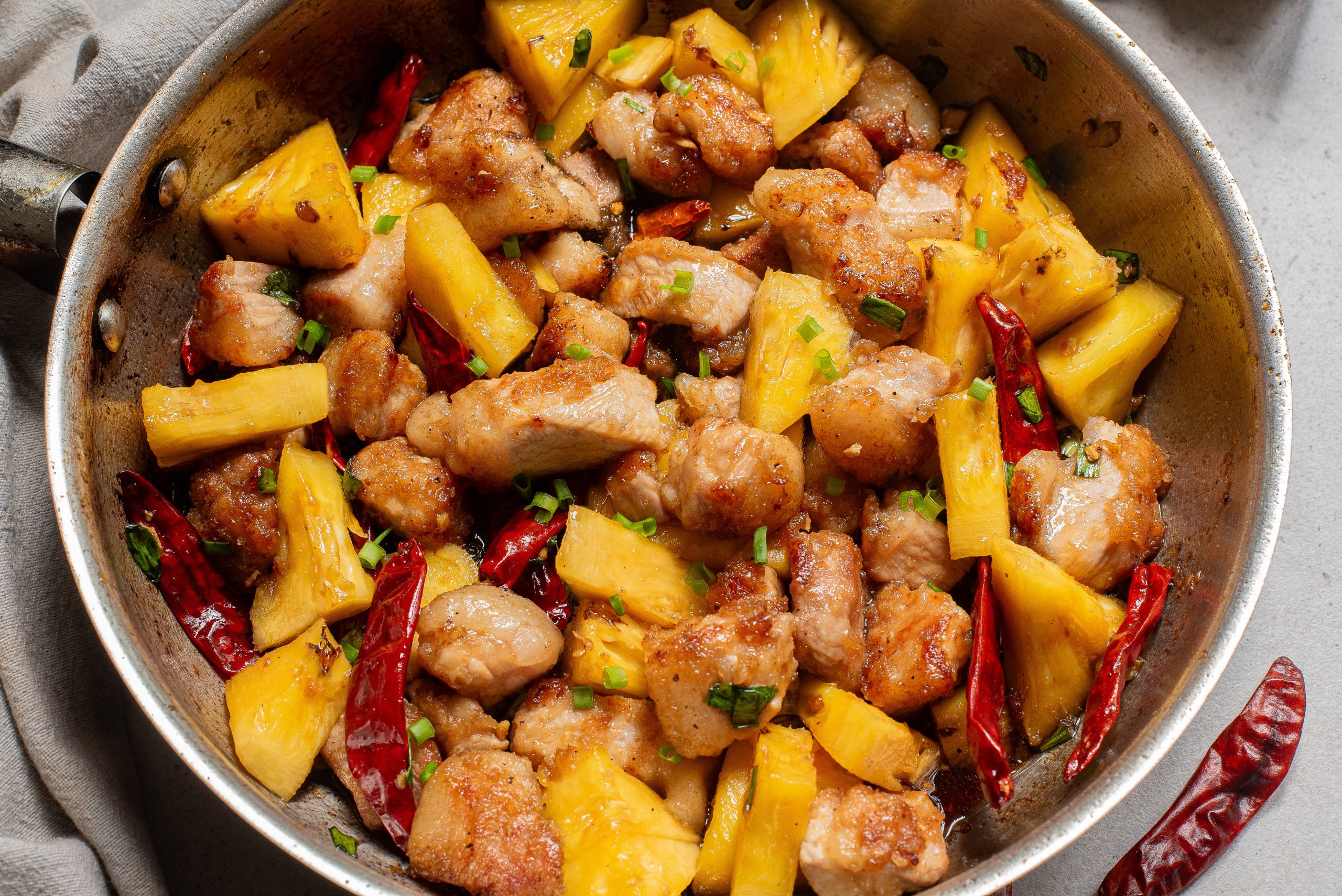 A skillet with Stovetop Honey Pineapple Pork is garnished with chopped green herbs.